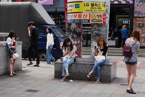 Three girls look at their smartphones while sitting or standing on the street
