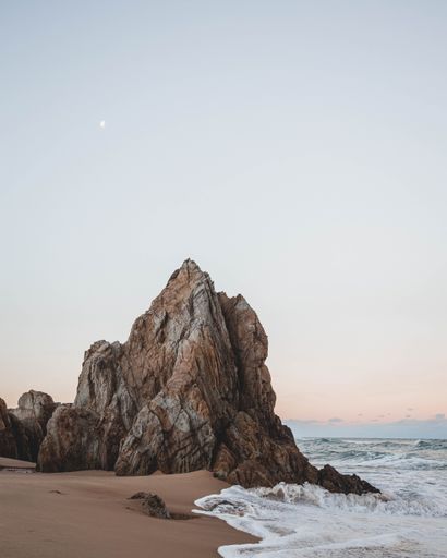 A vertical shot of an idyllic sandy coast with rocky cliffs at sunset