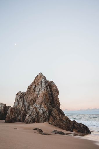 A vertical shot of an idyllic sandy coast with rocky cliffs at sunset