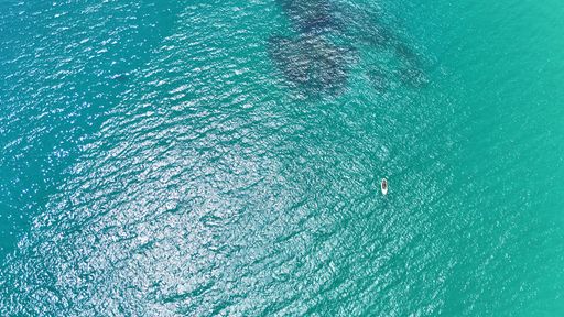 Aerial view of a small boat floating in the clear turquoise waters of the ocean on a sunny day.