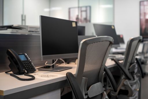 Modern office workspace featuring computer monitors, office chairs, and a desk phone.