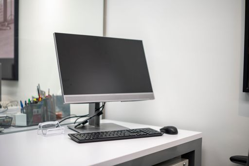 Modern office workspace with a computer monitor, keyboard, and mouse on a white desk.