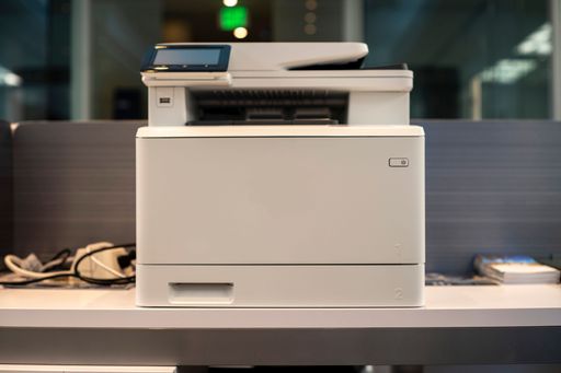 A modern office printer on a desk with blurred background.