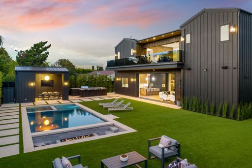 Modern luxury home exterior with swimming pool, lounge chairs, and outdoor dining area at sunset.