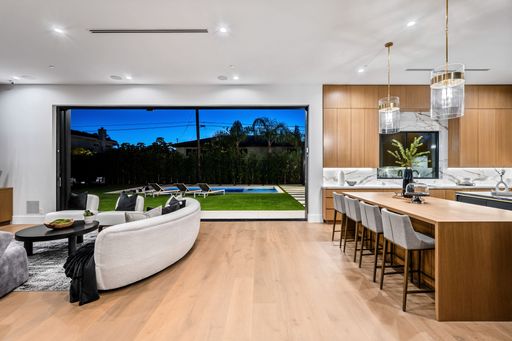 Modern open-plan living room and kitchen with view of outdoor pool and garden.