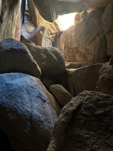 A view of large rocks inside a cave with natural light filtering through the opening above.