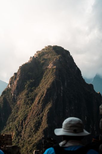 Tourists viewing the iconic Huayna Picchu mountain at Machu Picchu, Peru under a cloudy sky.