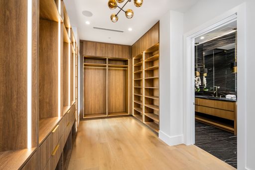 Modern walk-in closet with wooden shelves and drawers, leading to a luxurious bathroom with black marble tiles and gold fixtures.