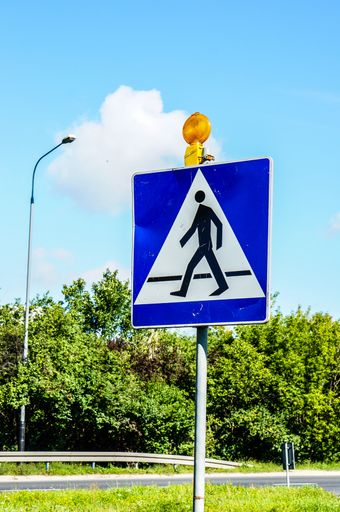 A vertical shot of a Pedestrian crossing traffic sign with a cloudy blue sky in the background