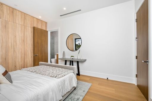 A modern bedroom with wooden accents, a large bed, and a minimalist desk with a round mirror on the wall.