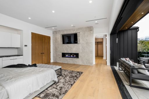 Modern bedroom with a fireplace, flat-screen TV, and open balcony with outdoor seating.