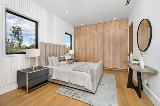 Modern bedroom interior with wooden accents, large bed, and natural light from two windows.