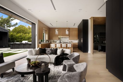 Modern open-concept living room and kitchen with large windows and outdoor seating area, featuring contemporary furniture and natural light.