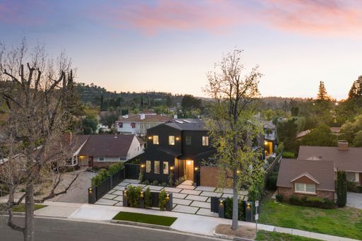 Modern black house in a suburban neighborhood at sunset with a clear sky and surrounding greenery.