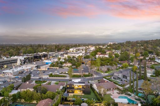 Aerial view of a suburban neighborhood with houses, greenery, and a sunset sky.