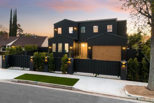 Modern black house with wooden accents and a well-manicured lawn at sunset in a suburban neighborhood.