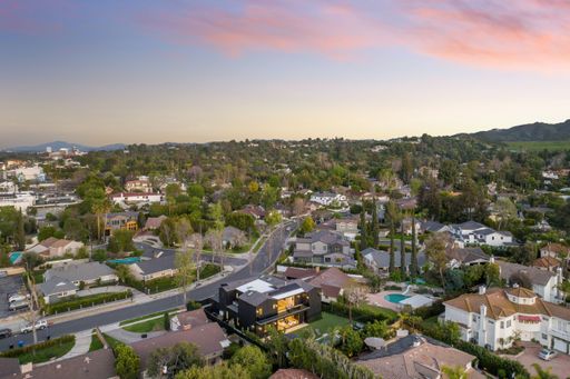 Aerial view of a suburban neighborhood at sunset with green trees and mountains in the background.