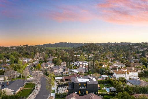 Aerial view of a suburban neighborhood with houses, trees, and a distant mountain range under a colorful sunset sky.