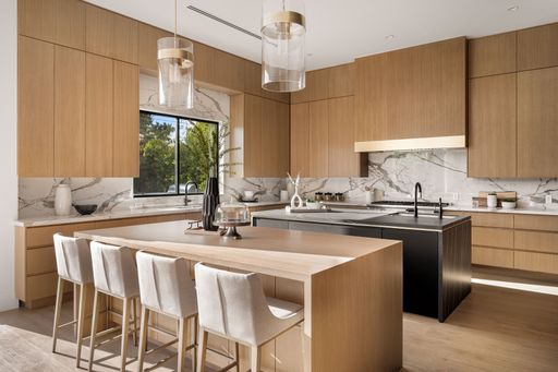 Modern kitchen interior with wooden cabinets, marble countertops, and an island with bar stools.