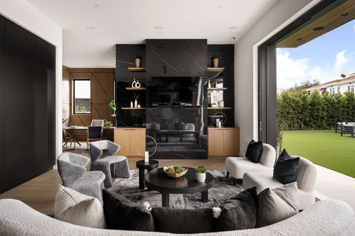 Modern living room interior with stylish furniture, black marble fireplace, and large windows opening to a green backyard.