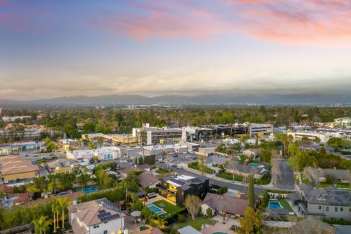 Aerial view of a suburban neighborhood with houses, buildings, and greenery under a colorful sky during sunset.