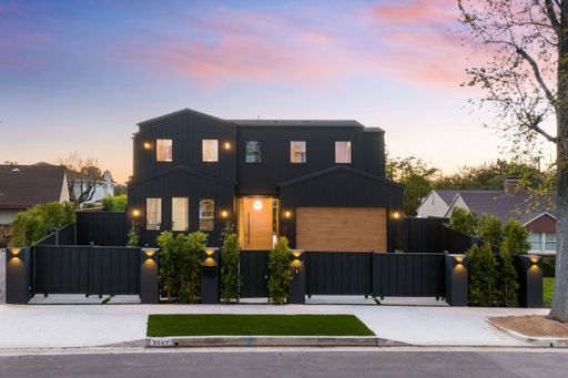 Modern two-story black house with a wooden door, fenced yard, and evening sky in a suburban neighborhood