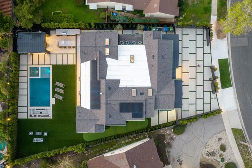 Aerial view of a modern house with a swimming pool and patio area in a suburban neighborhood.