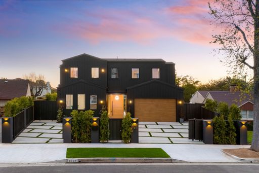 Modern black house with wooden accents and well-lit exterior at dusk in a suburban neighborhood.