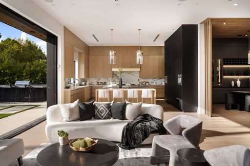Modern open-concept living room and kitchen with stylish furniture and large windows overlooking a garden.