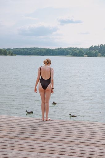 A vertical shot of a Caucasian blonde female in a black swimsuit looking at the ducklings in the lake