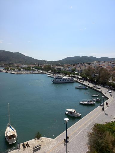 A scenic view of a coastal town with boats docked at the harbor and mountains in the background on a sunny day.