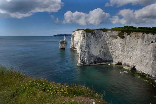 A scenic view of Old Harry Rocks, chalk formations on the Jurassic Coast in Dorset, England, under a partly cloudy sky.