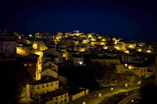 A night view of a hillside town with illuminated houses and a clear dark sky.