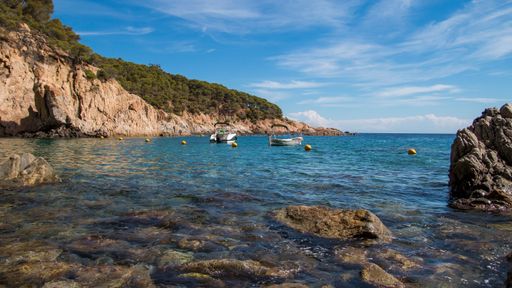 A view of a beautiful Tamariu with a blue sea and boats in it near the cliffs and hills in Spain