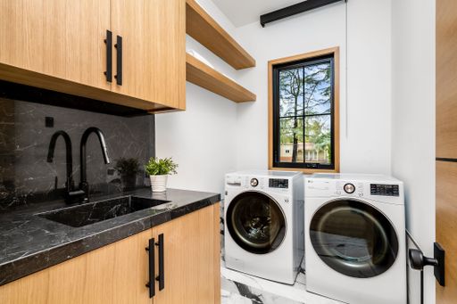 Modern laundry room with wooden cabinets, black countertop, and front-loading washer and dryer next to a window.