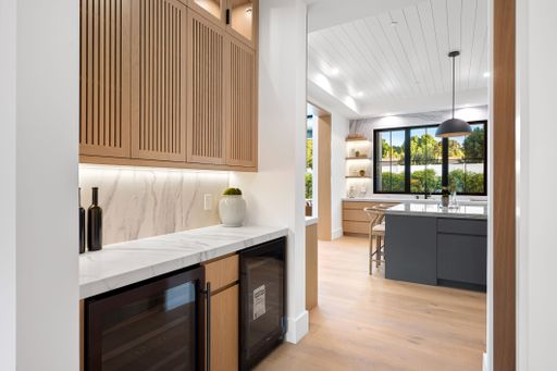 Modern kitchen interior with wooden cabinets, marble countertops, and large windows offering a view of greenery.