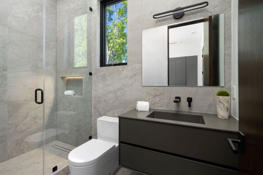 Modern bathroom with a sleek design featuring a glass shower, large mirror, and natural light from a window.