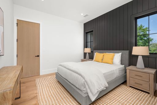 Modern bedroom with a grey bed, yellow pillows, wooden furniture, and black accent wall with windows.