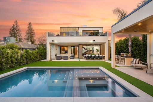 Modern luxury home with a swimming pool and outdoor seating area at sunset.