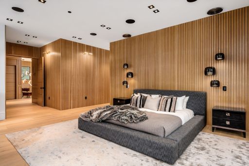 Modern bedroom interior with wooden panel walls, cozy bed, and stylish lighting fixtures.