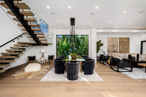 Modern open-concept living room and dining area with a wooden staircase, large window, and stylish furniture.