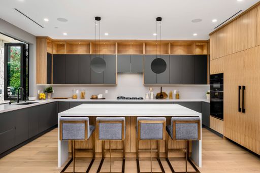 Modern kitchen interior with wooden cabinets, grey countertops, and a central island with bar stools.