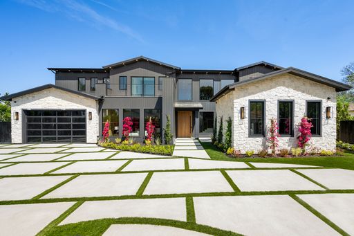 Modern luxury house with a spacious driveway and landscaped garden under a clear blue sky.