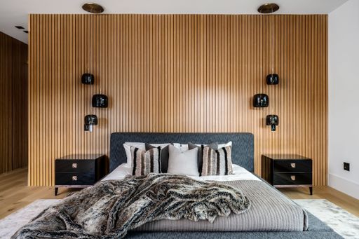 Modern bedroom interior with wooden slatted wall, black pendant lights, grey bed, and stylish decor.