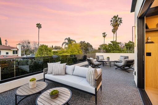 A modern outdoor patio with stylish furniture and a beautiful sunset sky view, surrounded by greenery and palm trees.