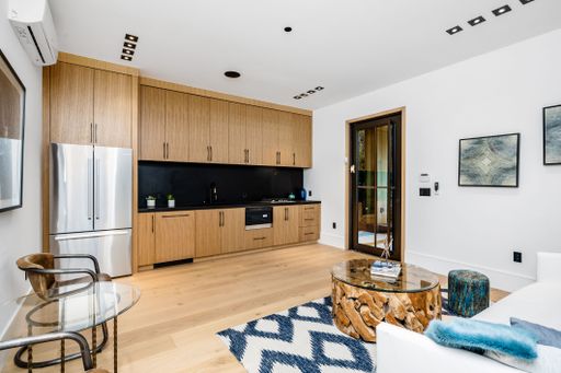 Modern kitchen and living room with wooden cabinets, stainless steel appliances, glass coffee table, and contemporary decor.