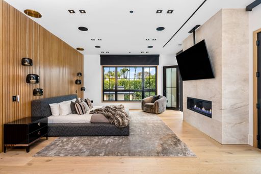 Modern bedroom interior with wood panel accent wall, cozy bed, large window, and contemporary fireplace.