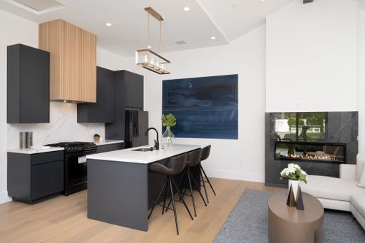 Modern kitchen and living area with sleek black cabinetry, white countertops, and a fireplace, featuring contemporary decor and a large painting.