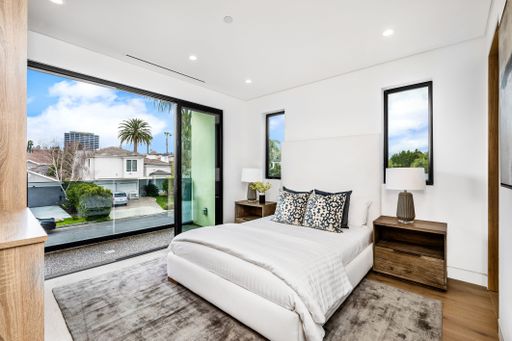 Modern bedroom interior with large windows offering a view of suburban houses and palm trees.