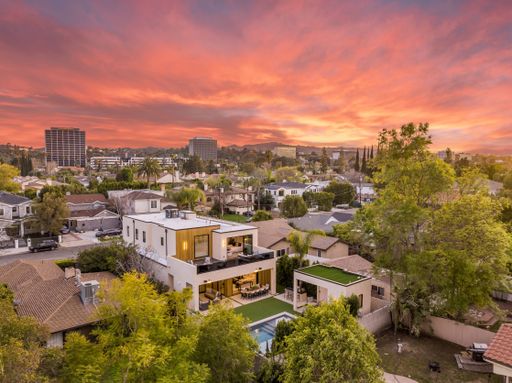 Aerial view of a suburban neighborhood with modern houses at sunset, showcasing a vibrant sky and lush greenery.